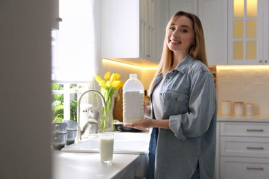 Photo of Young woman with gallon bottle of milk and glass at white countertop in kitchen