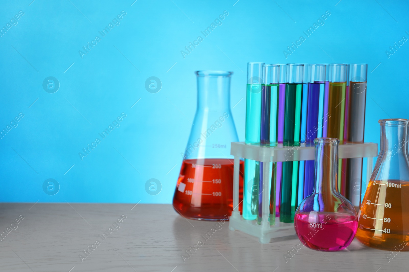 Photo of Different laboratory glassware with colorful liquids on wooden table against light blue background. Space for text