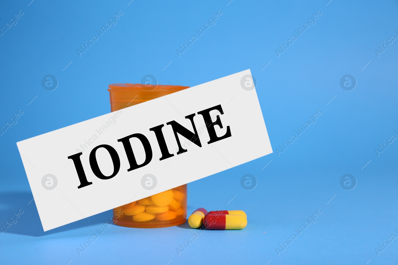 Photo of Paper note with word Iodine, bottle and pills on light blue background. Space for text