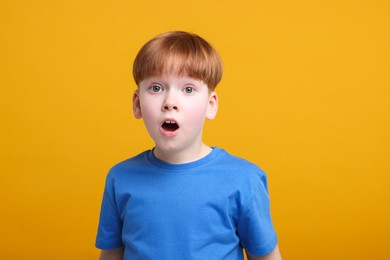 Portrait of surprised little boy on orange background