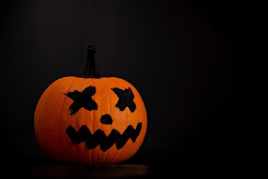Photo of Halloween celebration. Pumpkin with drawn face on table in darkness, space for text