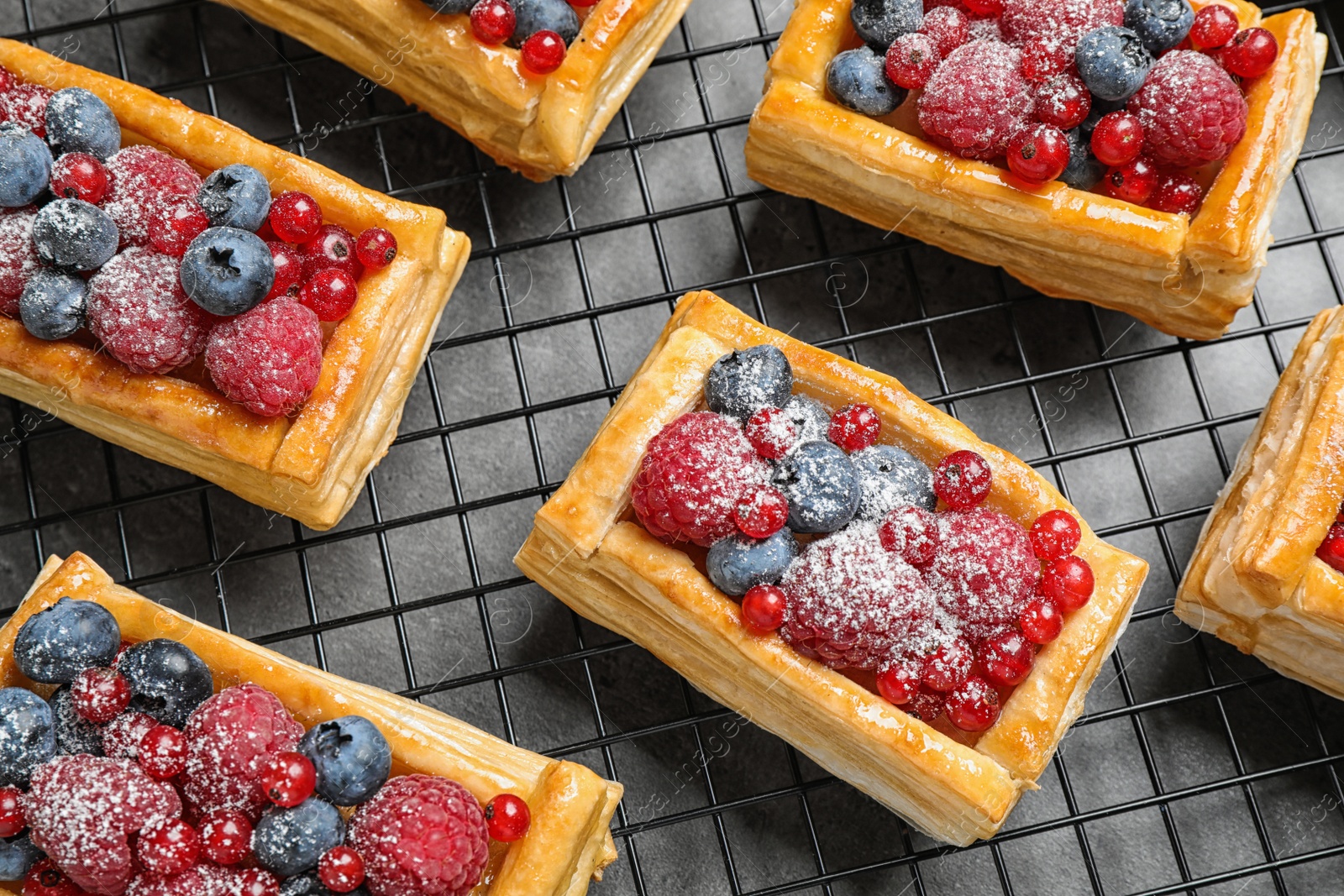 Photo of Cooling rack and fresh delicious puff pastry with sweet berries on grey table, above view