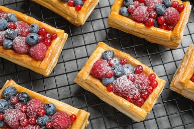 Photo of Cooling rack and fresh delicious puff pastry with sweet berries on grey table, above view