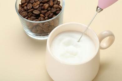 Whisking milk in cup with mini mixer (milk frother) on beige background, closeup