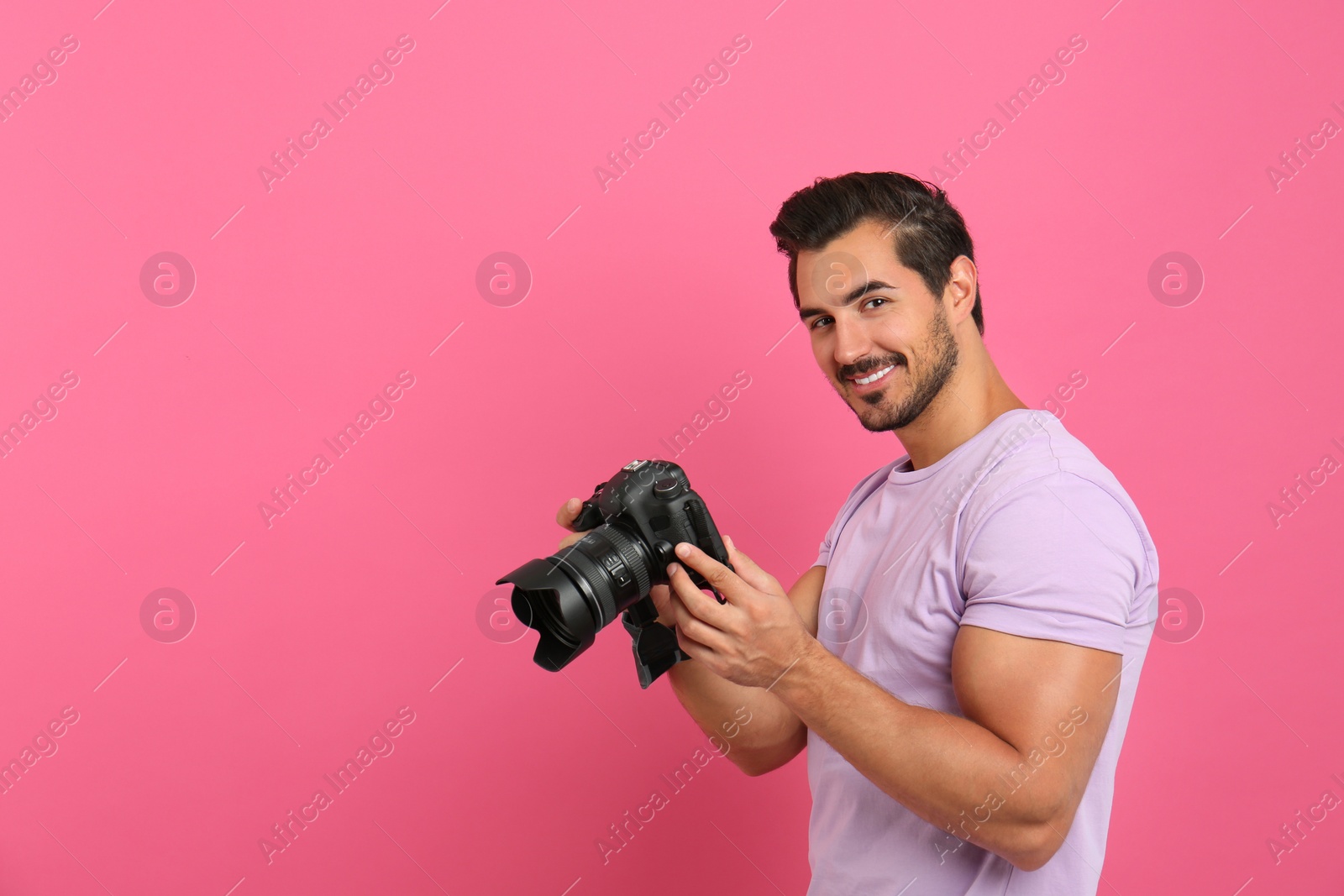 Photo of Young photographer with professional camera on pink background. Space for text