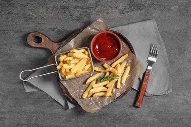 Photo of Tasty French fries, ketchup and rosemary on grey table, top view