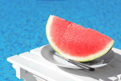 Photo of Slice of fresh juicy watermelon on white plate near swimming pool outdoors. Space for text