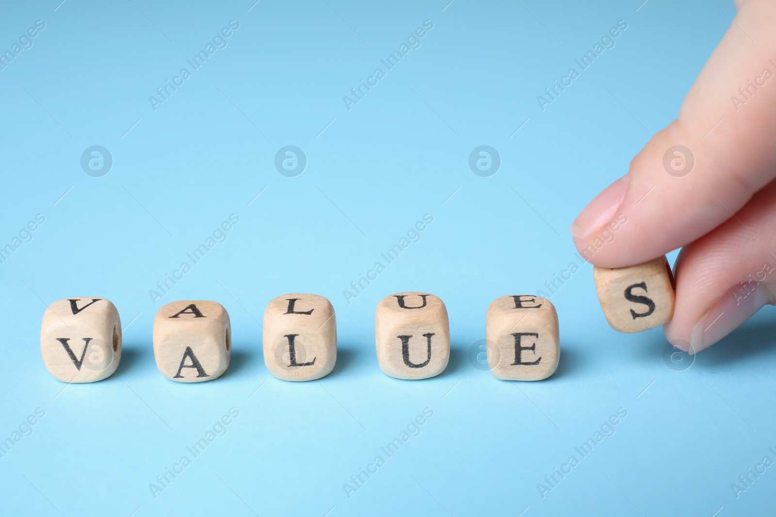 Photo of Woman making word VALUES with beads on light blue background, closeup