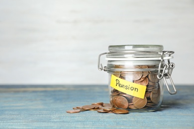 Photo of Coins in glass jar with label "PENSION" on table against light wall. Space for text