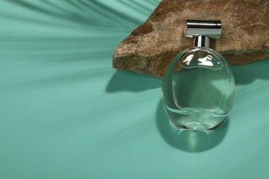 Photo of Luxury perfume in bottle and stone on turquoise background, above view. Space for text