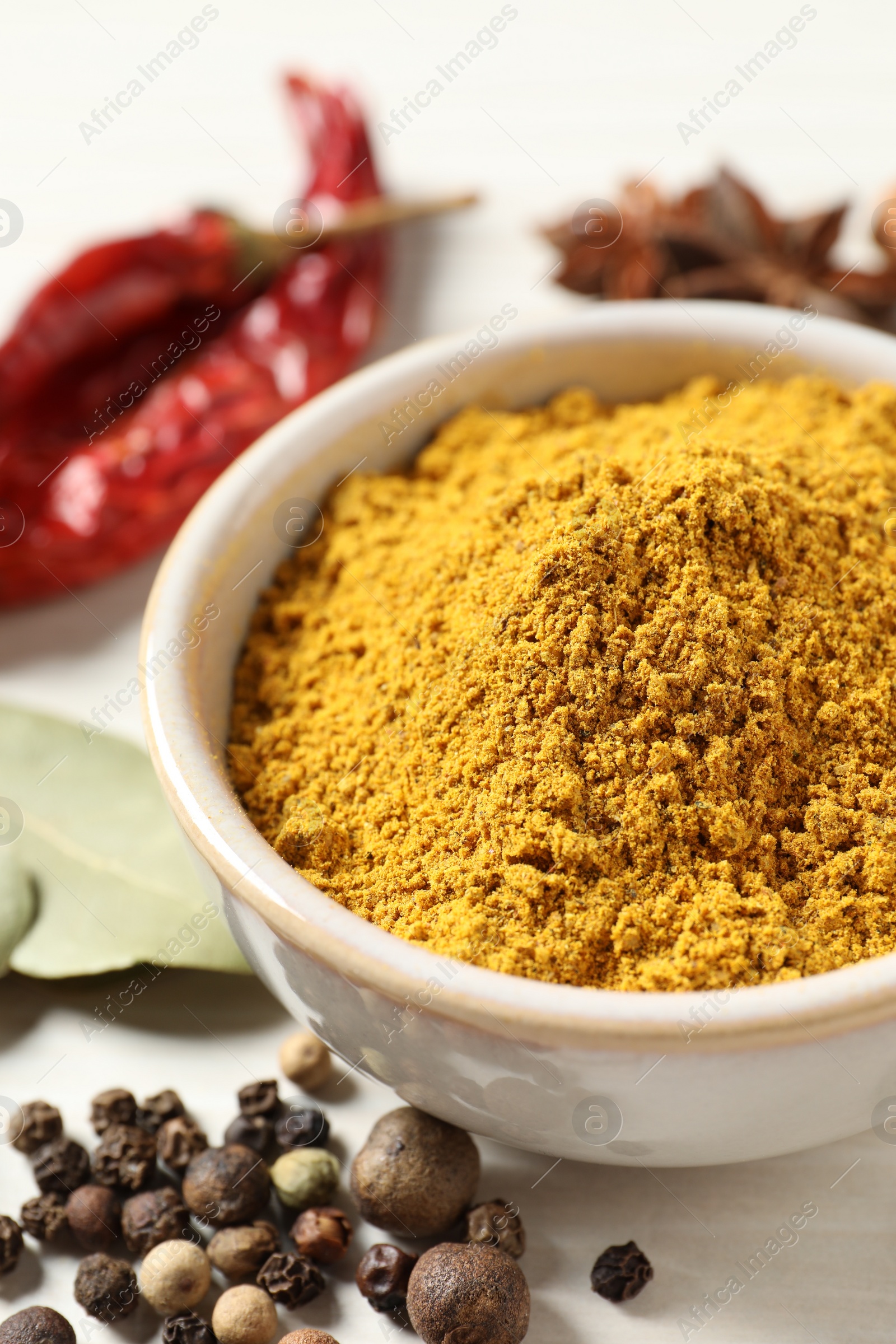 Photo of Curry powder in bowl and other spices on white wooden table, closeup