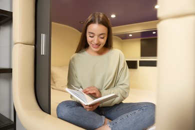 Photo of Happy young woman reading book in capsule of pod hostel