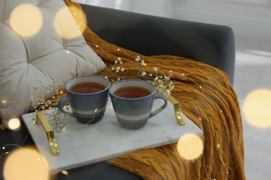 Marble tray with hot tea, flowers and fairy lights on sofa indoors