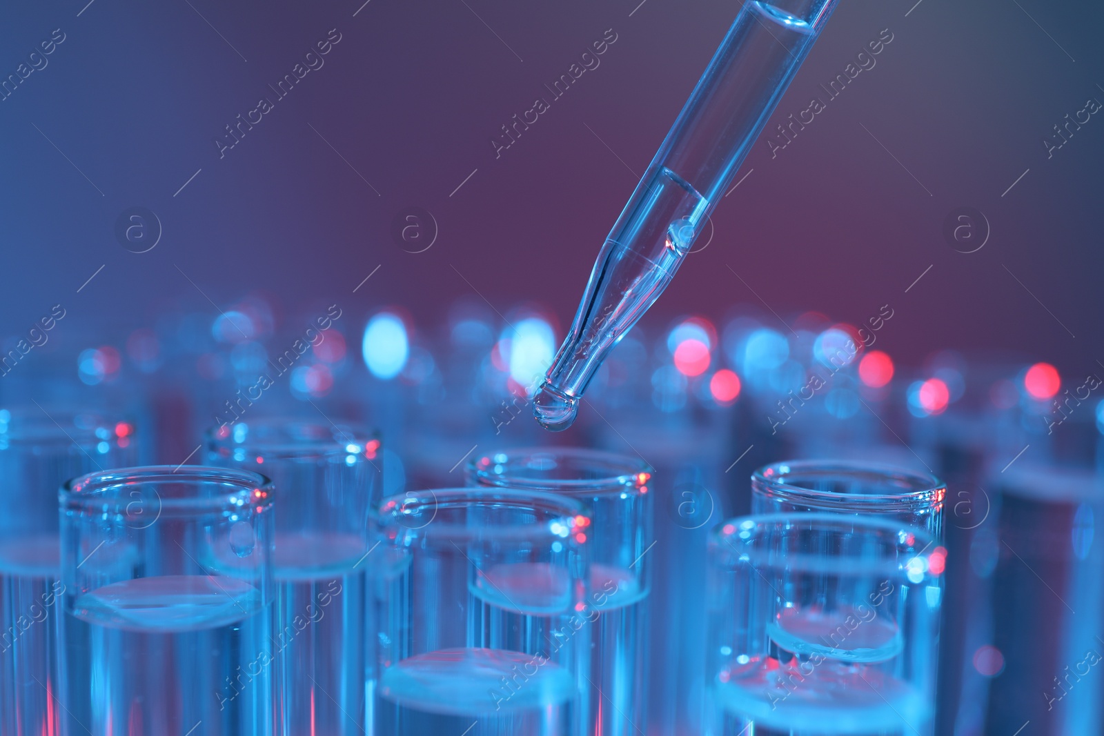 Photo of Dripping liquid from pipette into test tube on color background, closeup