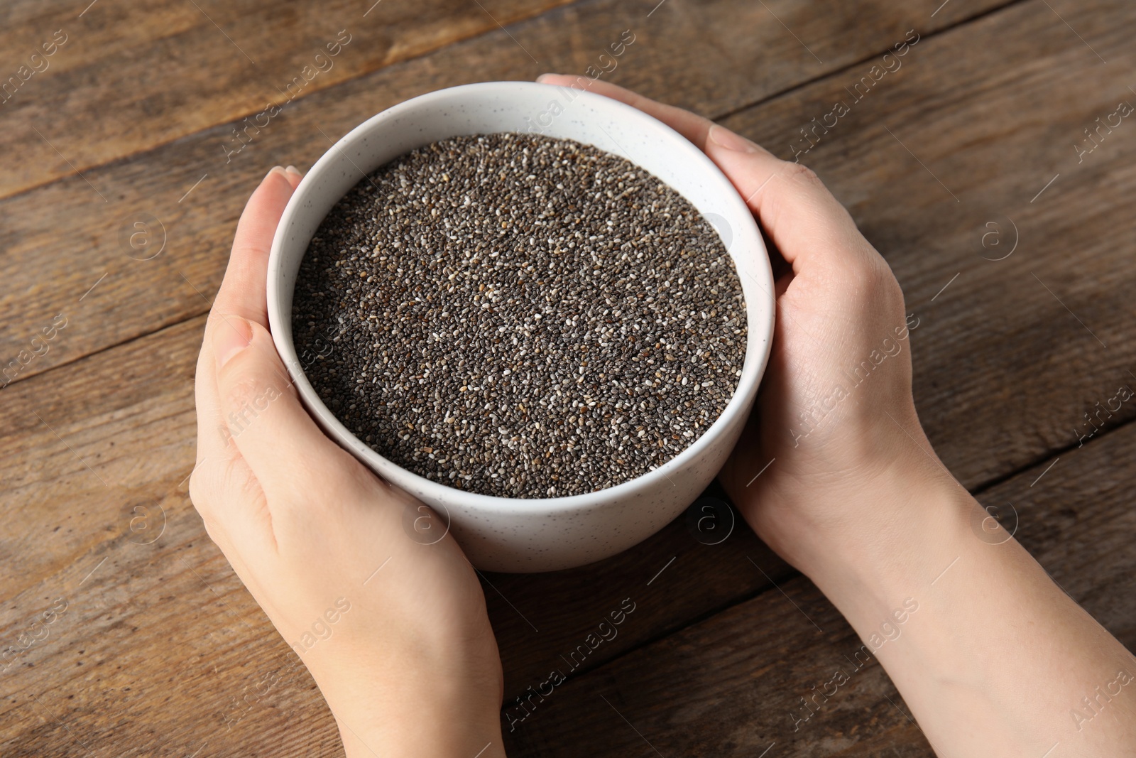 Photo of Woman holding bowl with chia seeds on wooden background, closeup