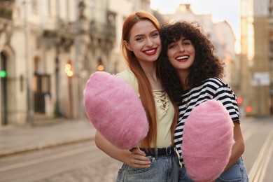 Photo of Happy friends with pink cotton candies on city street. Space for text