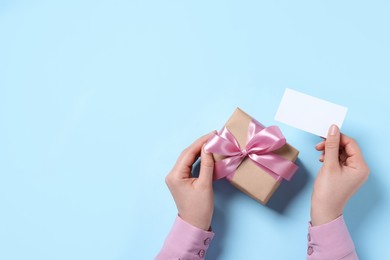 Photo of Woman with gift box and blank card on light blue background, top view. Space for text