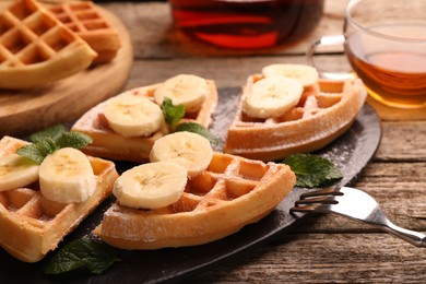 Photo of Tasty Belgian waffles with banana and mint on wooden table, closeup