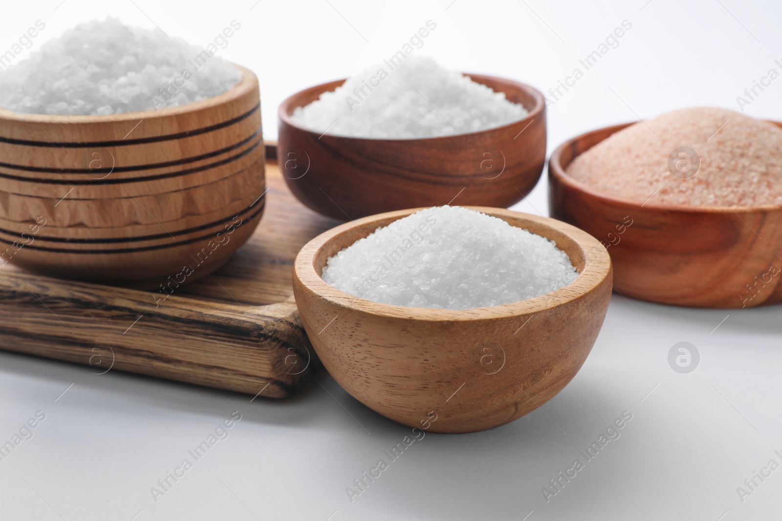 Photo of Different types of natural salt in wooden bowls on white background