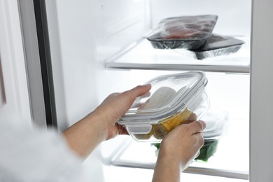 Photo of Young woman taking container with corn out of refrigerator, closeup