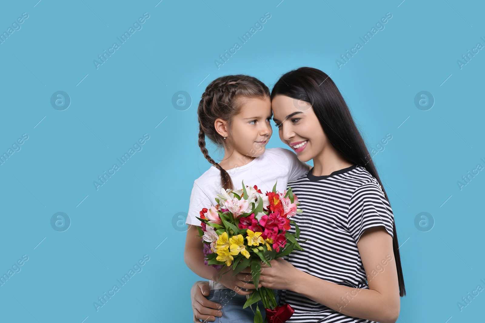 Photo of Happy woman with her daughter and bouquet of beautiful flowers on light blue background, space for text. Mother's day celebration