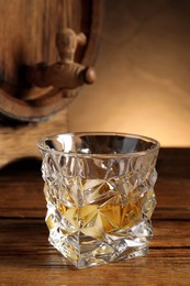 Glass of whiskey and wooden barrel on table, closeup