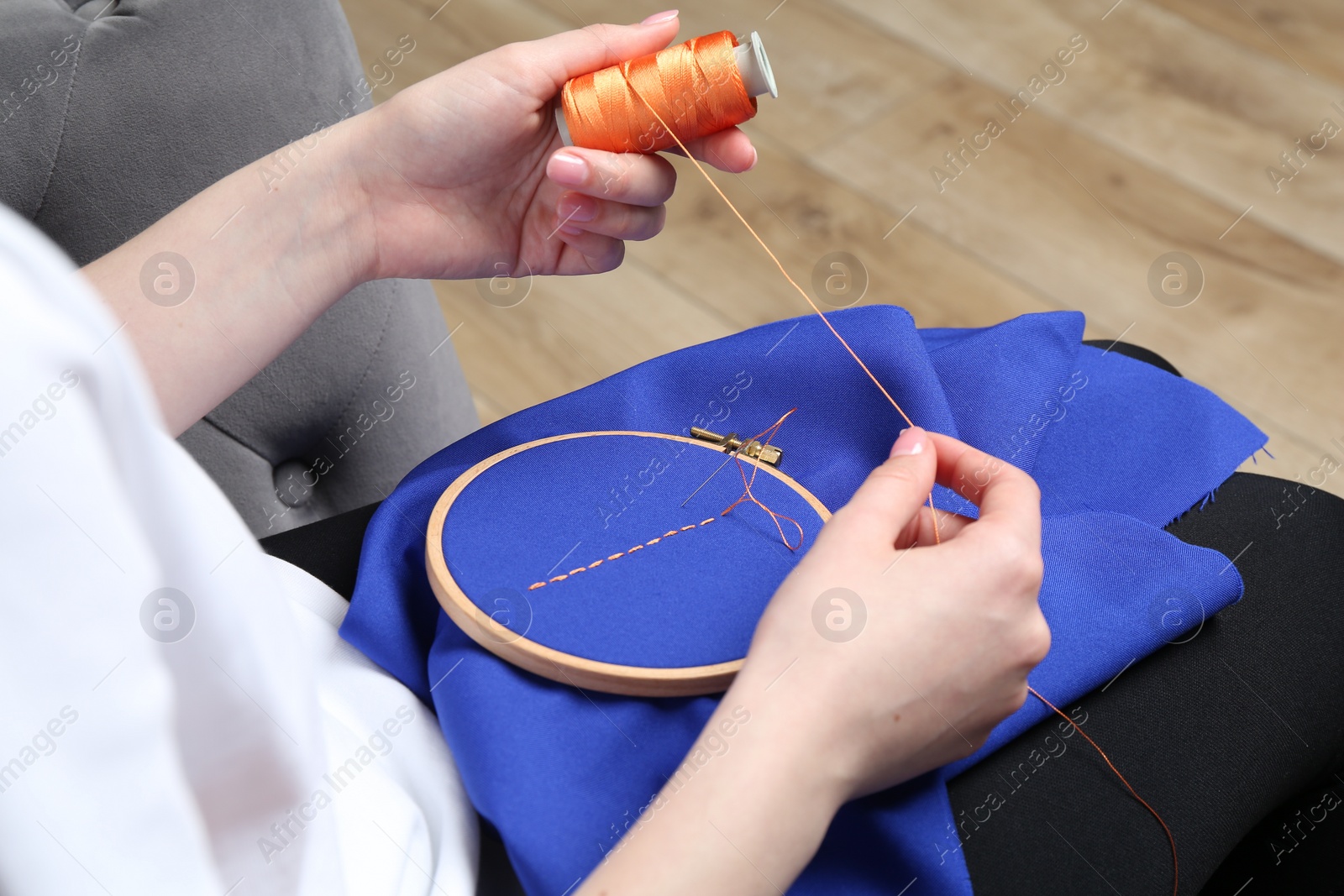 Photo of Woman with spool of thread embroidering on cloth at home, closeup