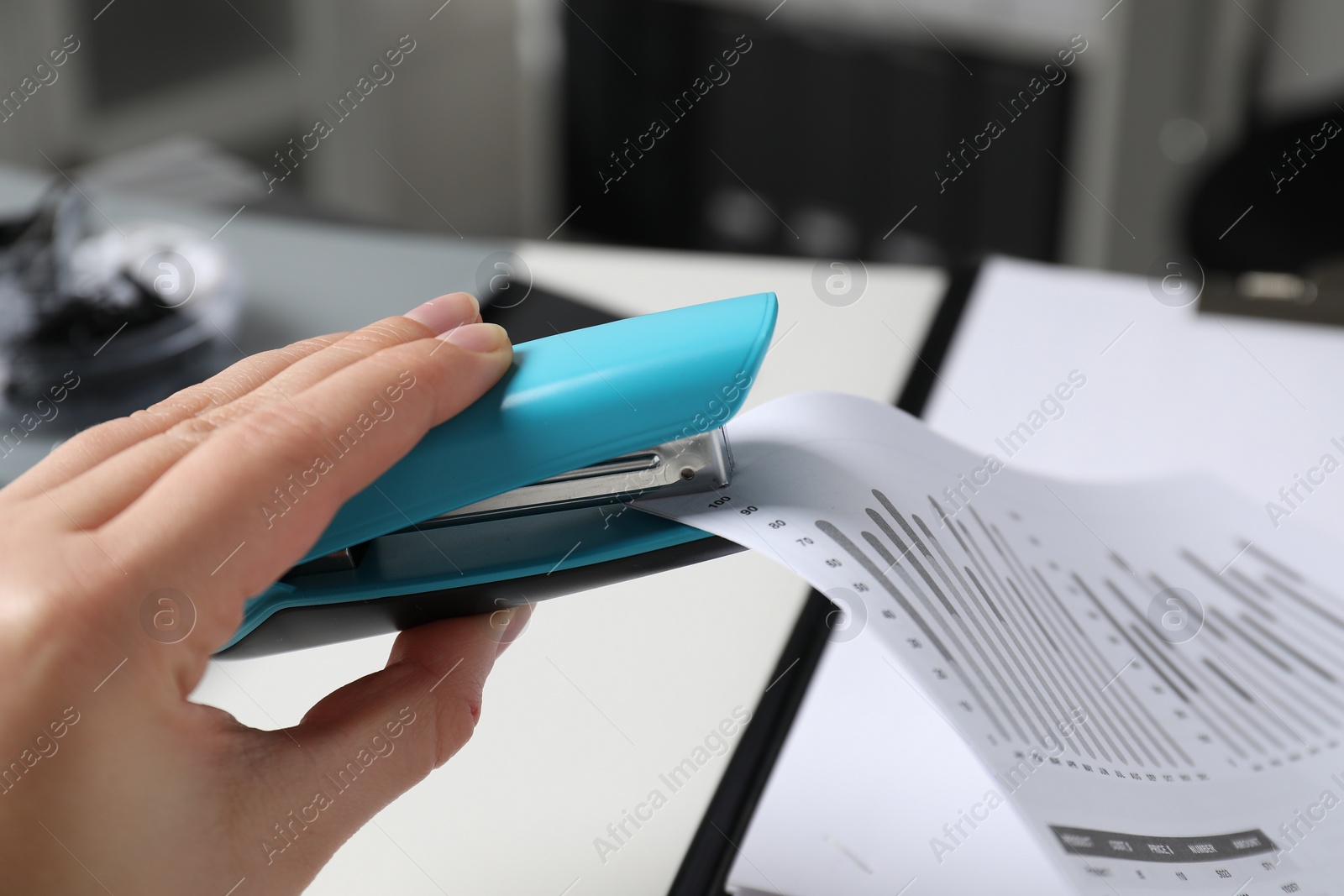 Photo of Woman with documents using stapler at white table indoors, closeup