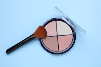 Photo of Contouring palette and brush on light blue background, top view. Professional cosmetic product