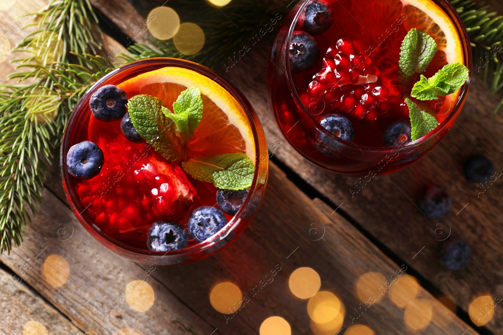 Photo of Aromatic Christmas Sangria drink in glasses and fir branches on wooden table, flat lay