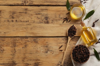 Photo of Essential oil and dried cloves on wooden table, flat lay. Space for text