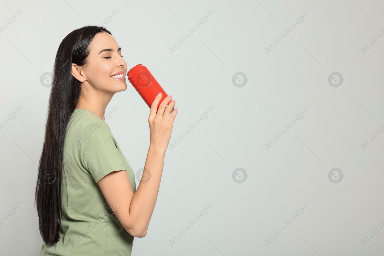 Photo of Beautiful happy woman holding red beverage can on light grey background. Space for text