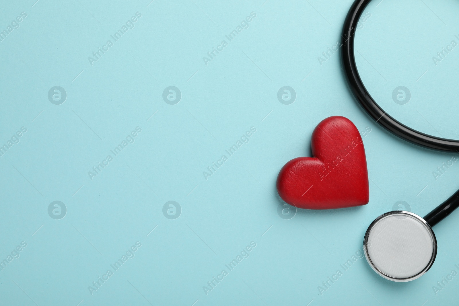 Photo of Stethoscope and red heart on light blue background, top view. Space for text