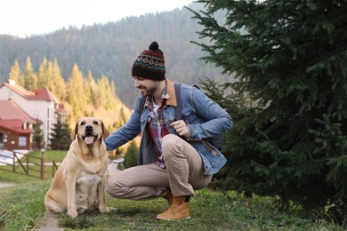 Photo of Happy man and adorable dog sitting on green grass in mountains. Traveling with pet