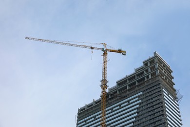 Construction site with tower crane near unfinished building, low angle view