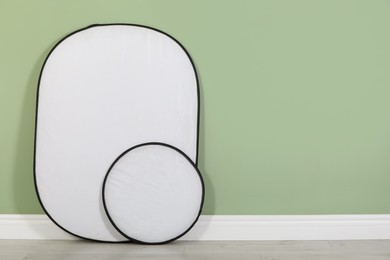 Photo of Studio reflectors near pale green wall in room, space for text. Professional photographer's equipment
