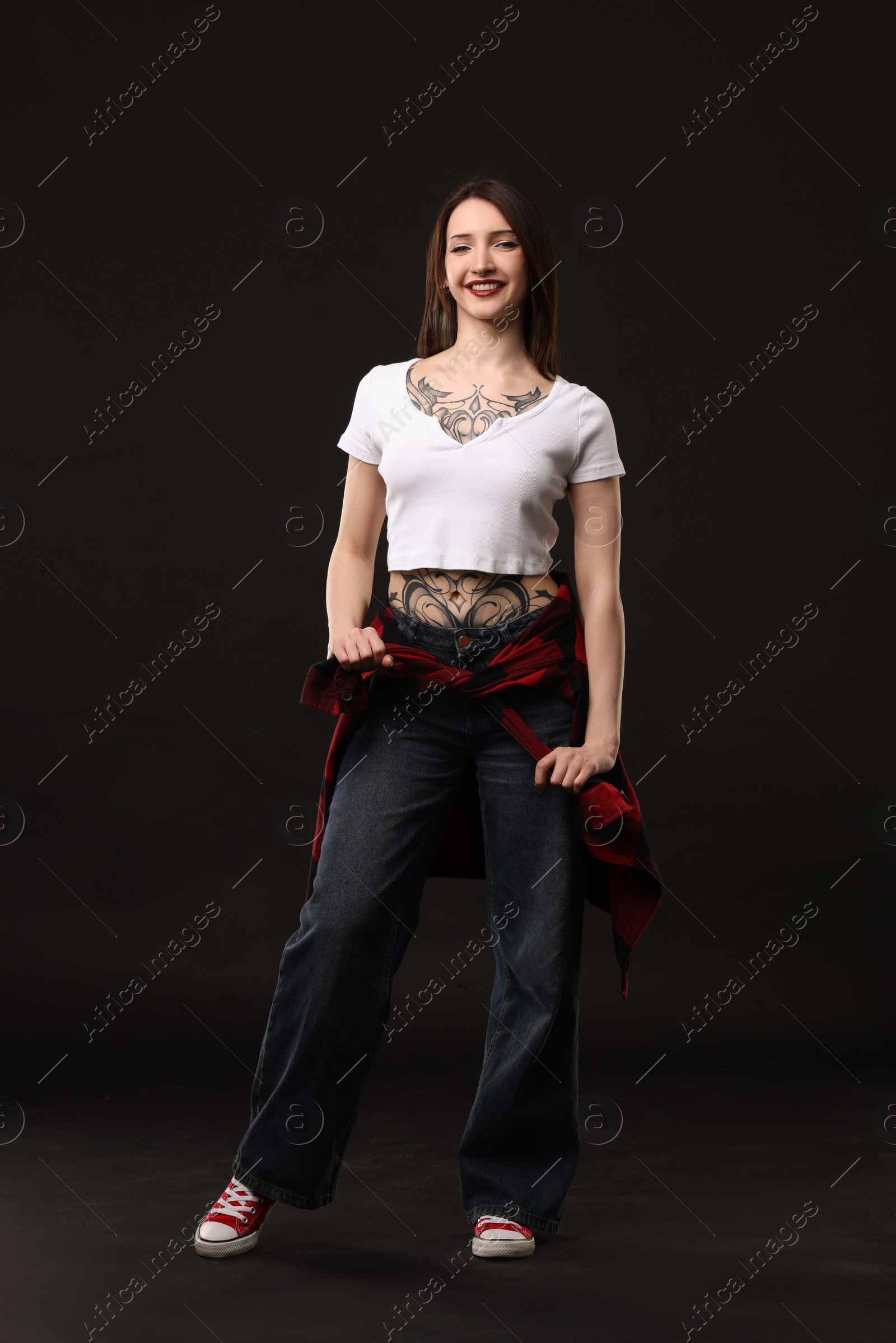 Photo of Full length portrait of smiling tattooed woman on black background