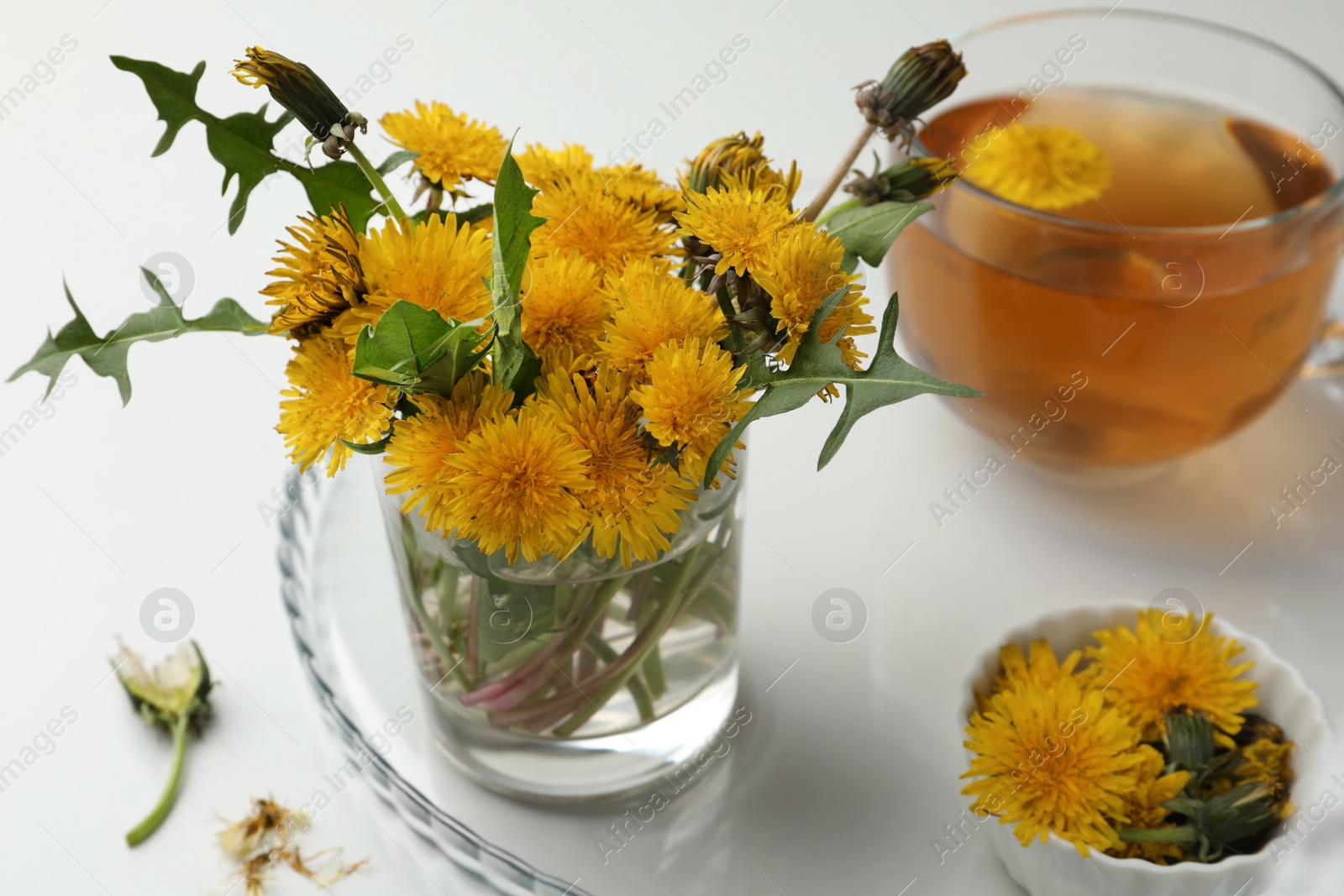 Photo of Beautiful dandelion bouquet and delicious fresh tea on white table