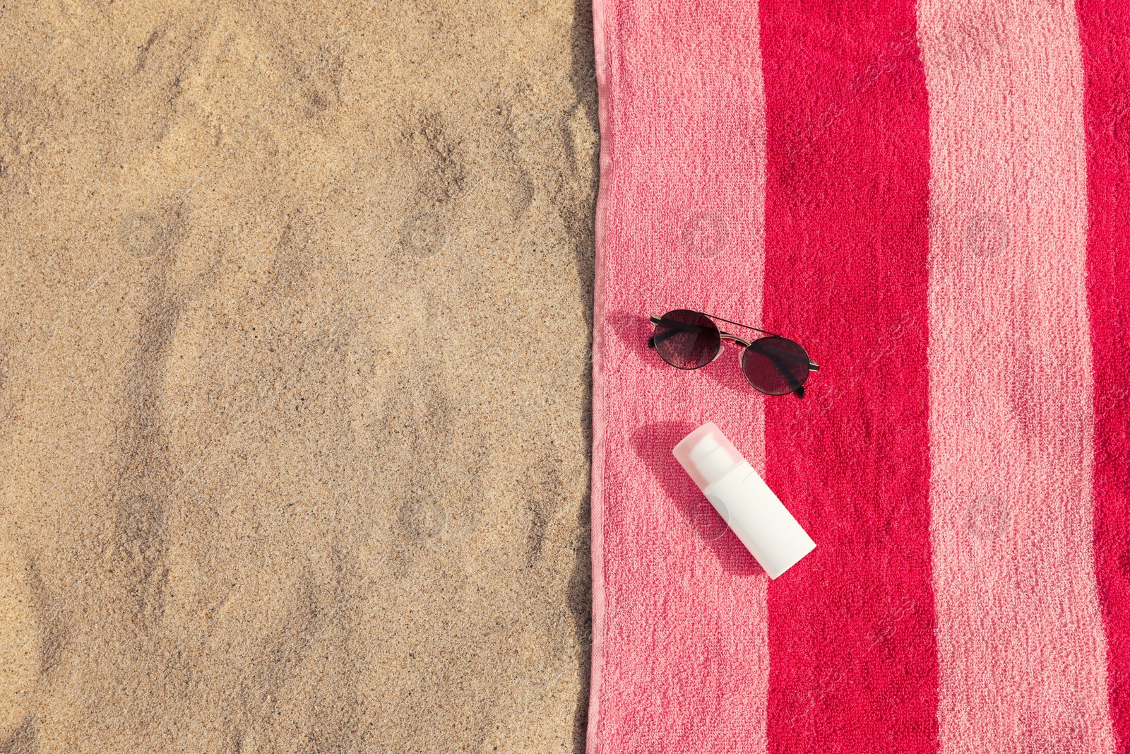 Photo of Beach towel with sunglasses and sunscreen on sand, flat lay. Space for text