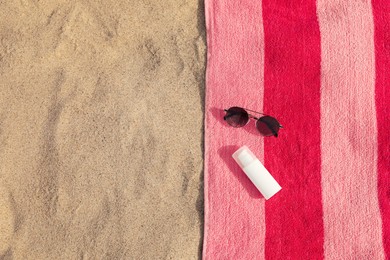 Beach towel with sunglasses and sunscreen on sand, flat lay. Space for text