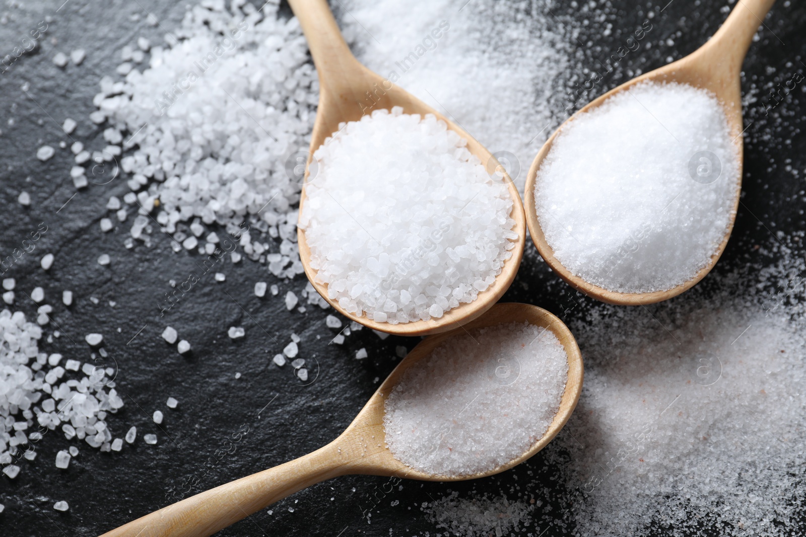 Photo of Organic salt in spoons on black table, closeup