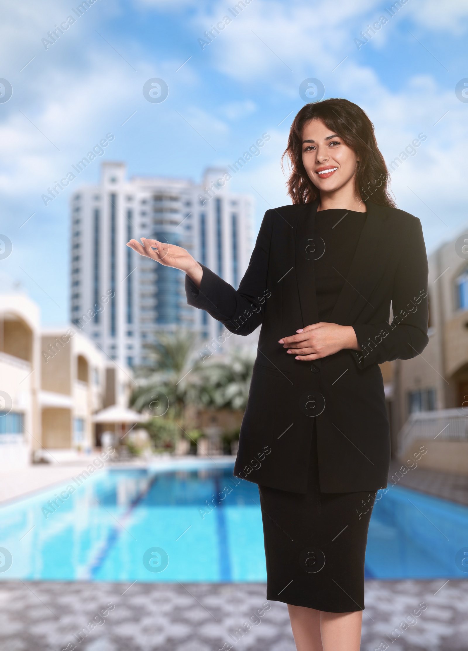 Image of Portrait of hostess in uniform and blurred view of modern luxury hotel with swimming pool on sunny day