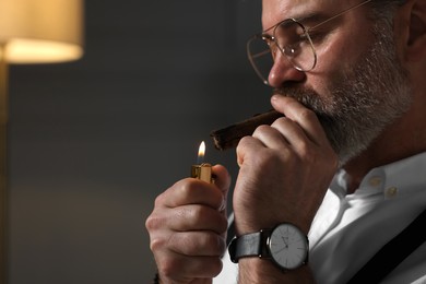 Bearded man lighting cigar indoors, closeup. Space for text