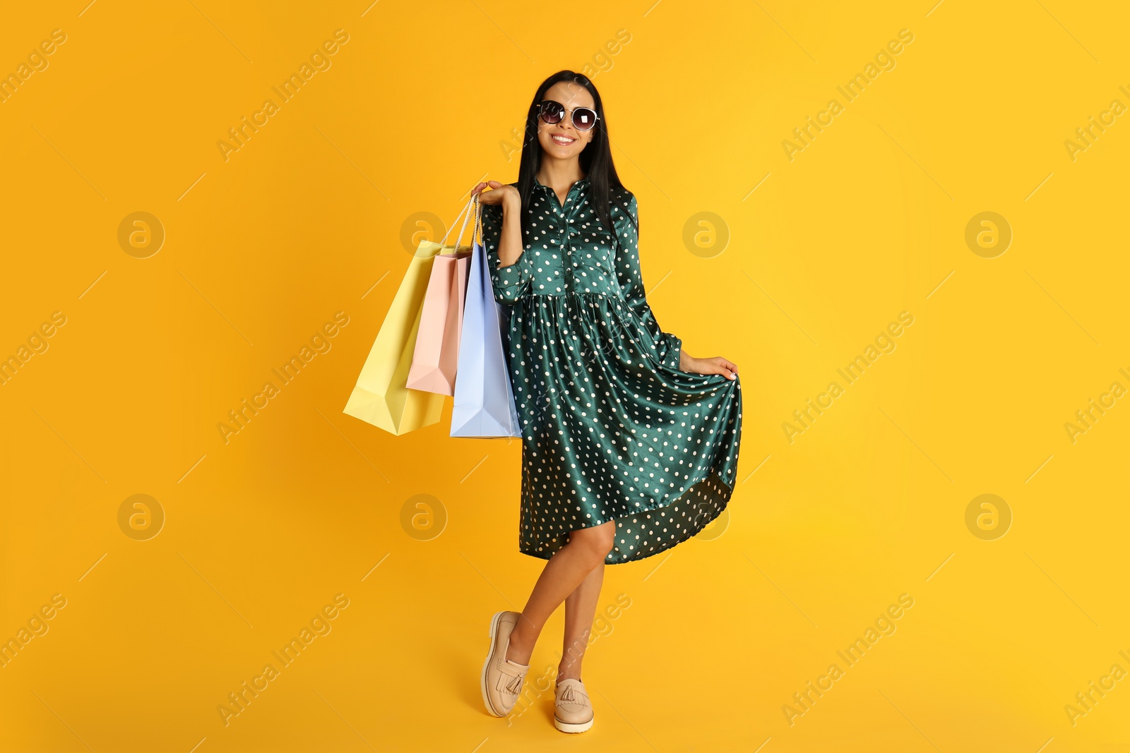 Photo of Beautiful young woman with paper shopping bags on yellow background