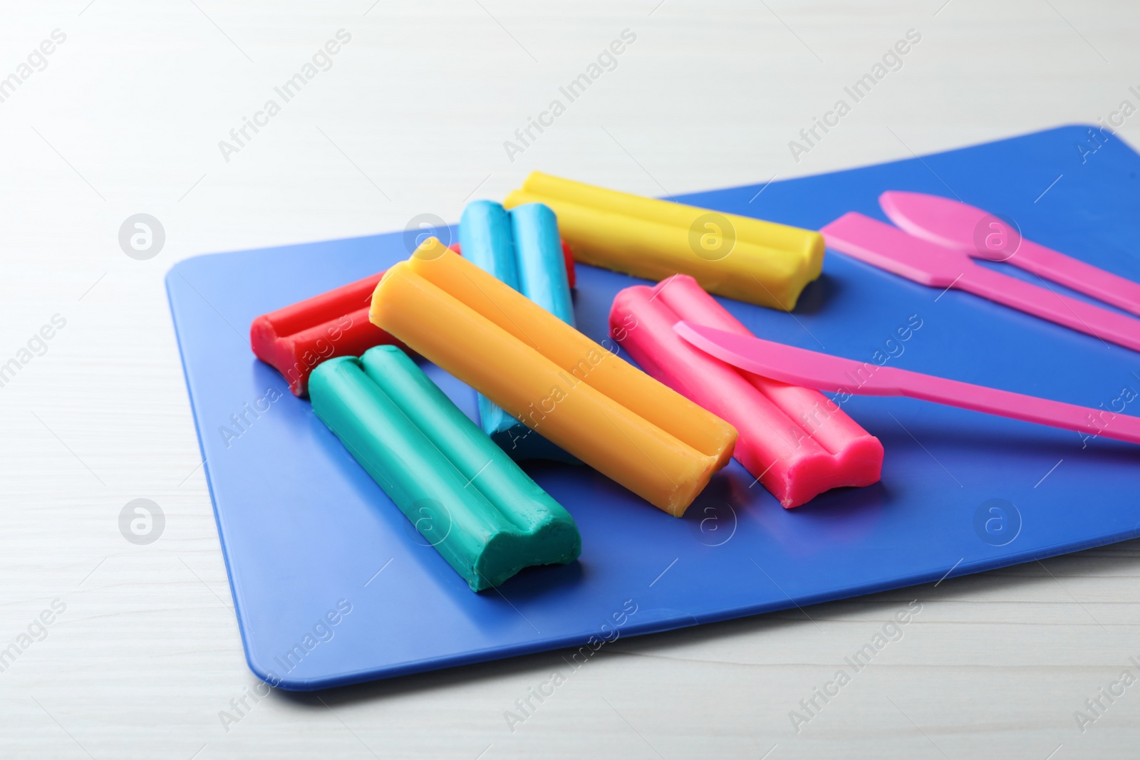 Photo of Many different colorful plasticine pieces with tools on white wooden table