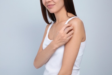 Young woman scratching shoulder on light background, closeup. Annoying itch