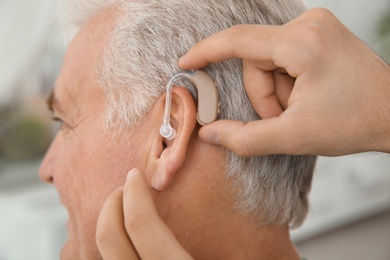 Young man putting hearing aid in father's ear indoors, closeup