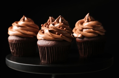Photo of Delicious chocolate cupcakes with cream and beads on black stand, closeup