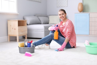 Photo of Young woman with cleaning supplies on carpet at home