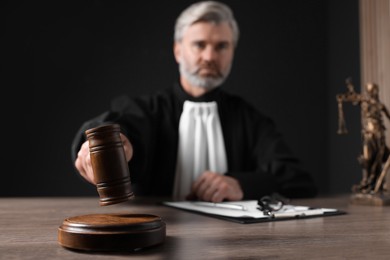 Photo of Judge with gavel and papers sitting at wooden table against black background, selective focus